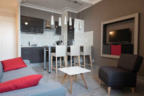 Séjour avec canapé, fauteuil et télévision, cuisine ouverte équipée en arrière-plan